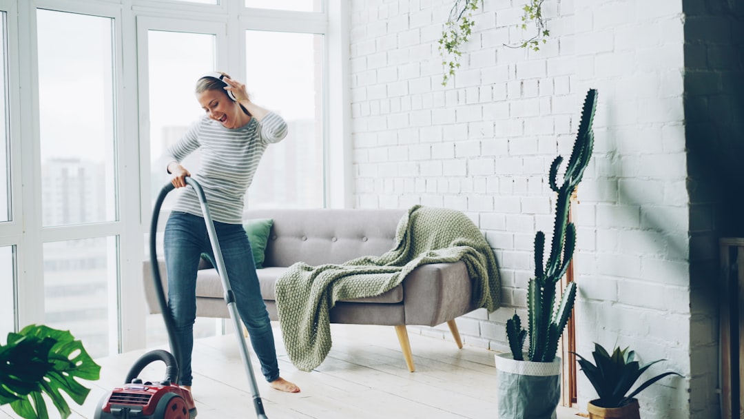 testimonials-img Cheerful blond housewife is using vacuum cleaner during routine clean-up at home, listening to music through headphones, singing and dancing. Technology and young people concept.
