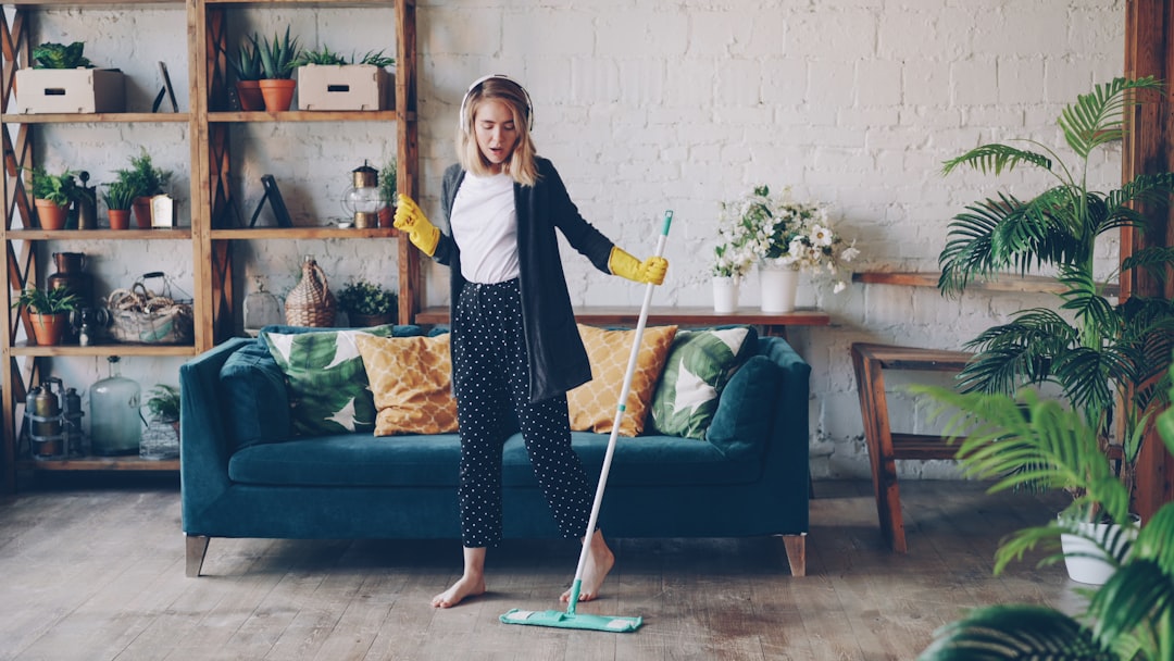 home-services-01 Attractive girl in headphones is listening to music and dancing wih mop during domestic work, she is mopping floor at home and having fun. Women, joy and modern houses concept.